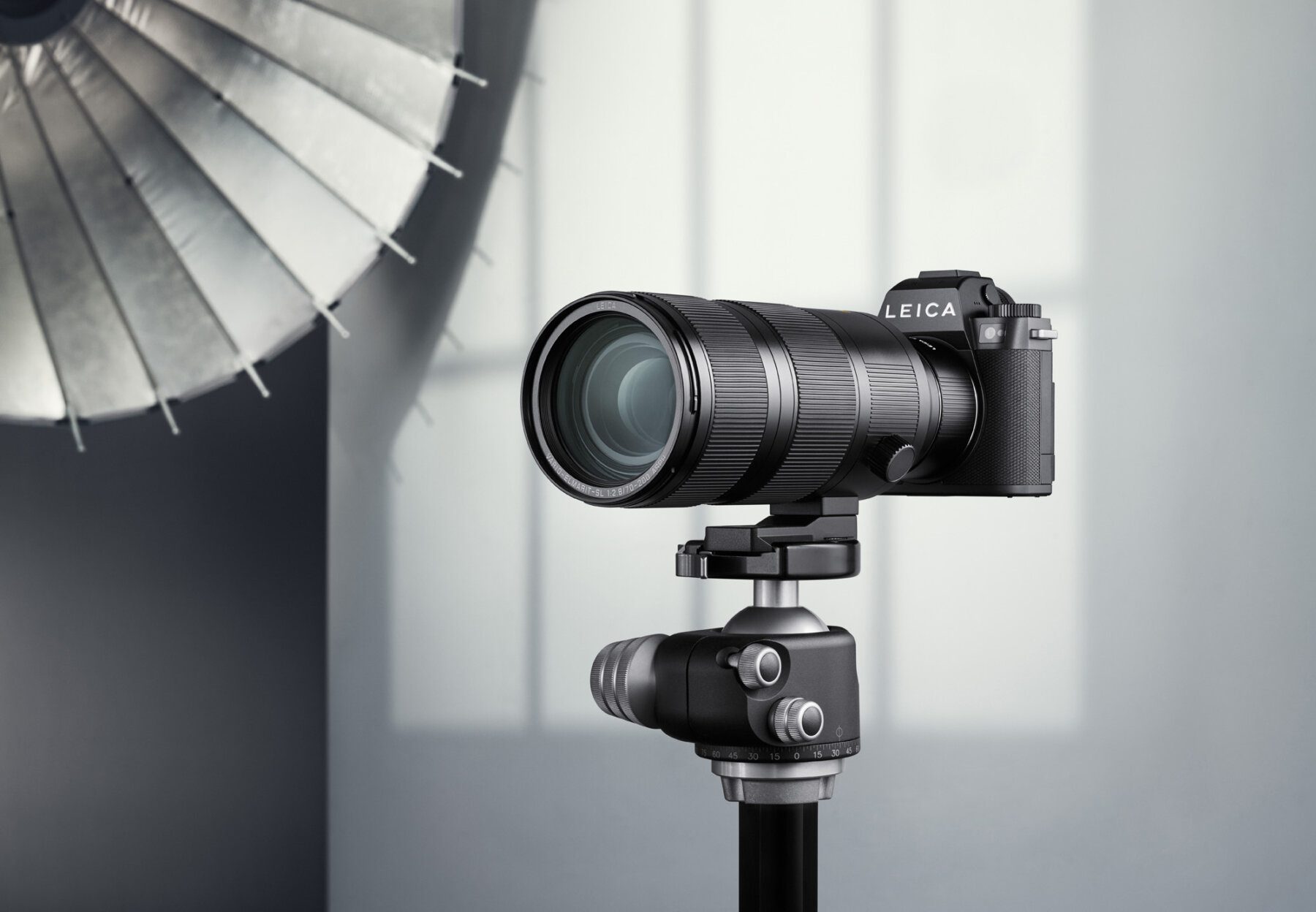 A Leica digital camera is mounted on a tripod with ball head in a still life photo set