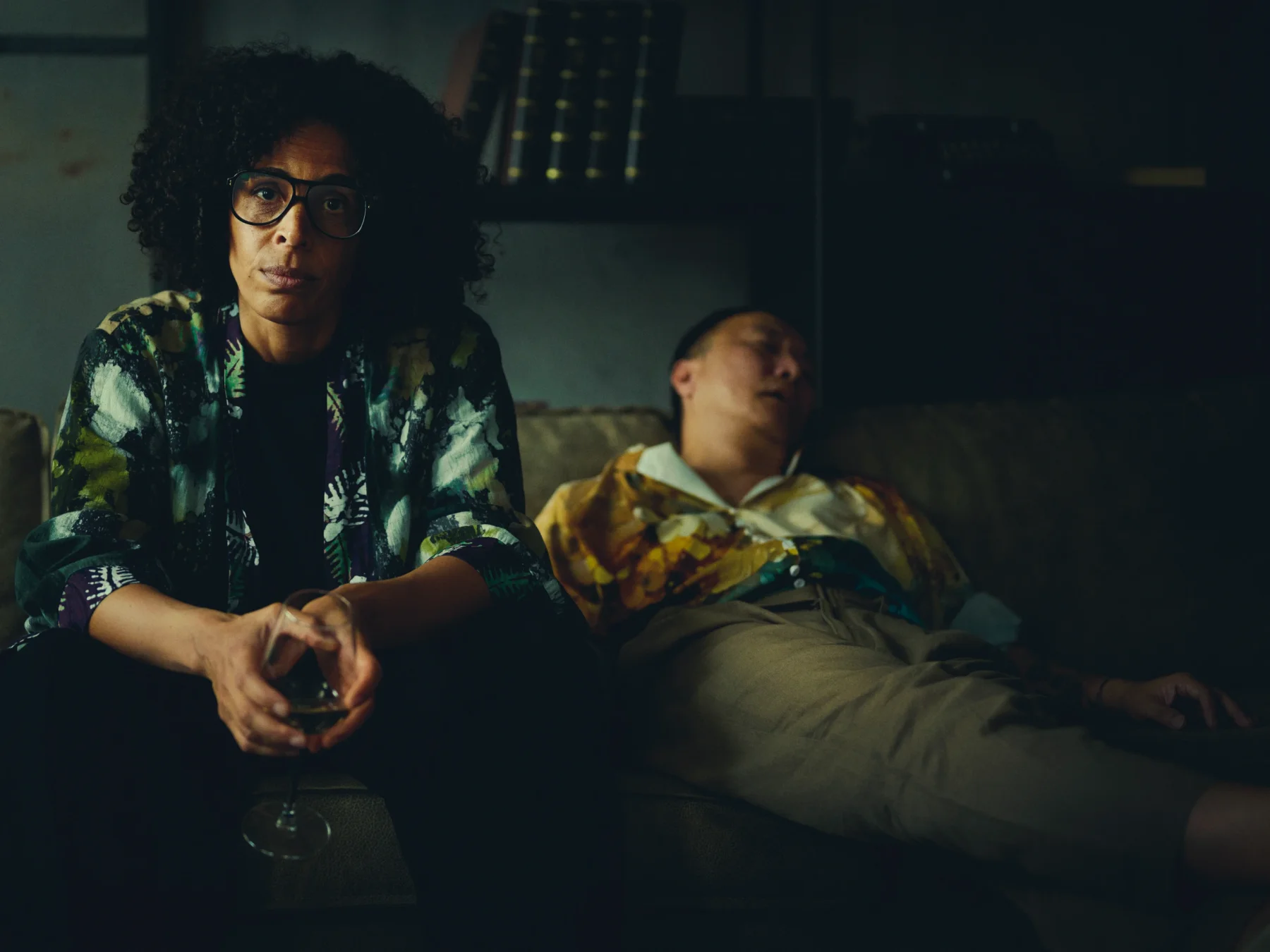 a woman sits on a couch next to a sleeping man