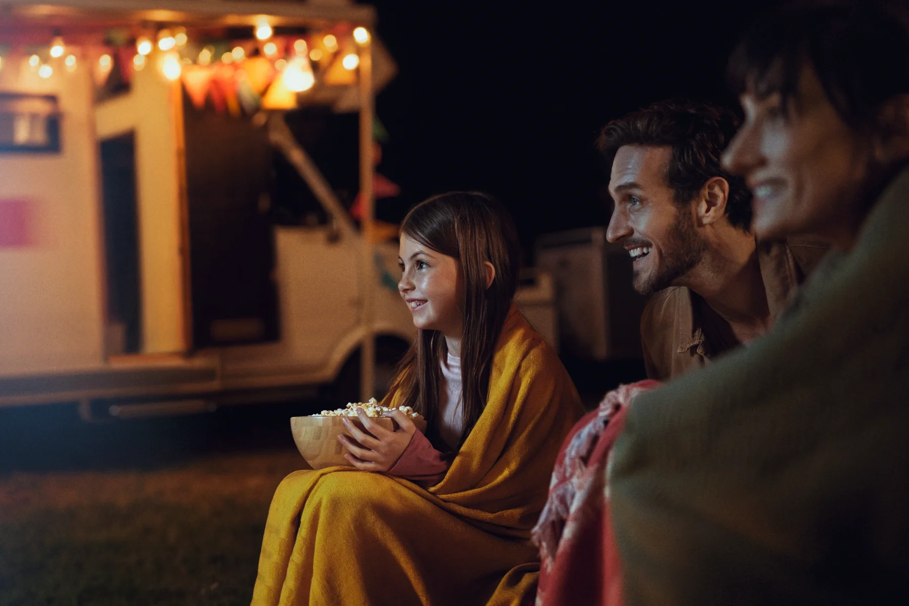 a family watches a movie outdoor in front of their caravan